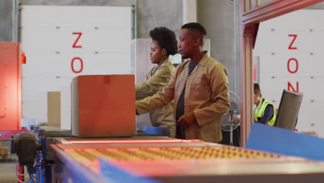 African-american-male-and-female-workers-with-boxes-on-conveyor-belt-in-warehouse