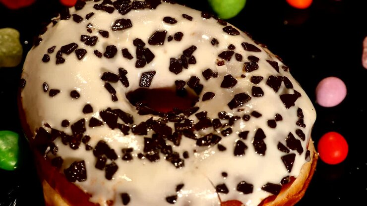 Ciambella glassata bianca con cioccolato, glassa o codette colorate, caramelle mou a strisce, confetti colorati con uvetta o arachidi all'interno su sfondo nero
