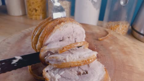 slow motion slider shot of slicing a roast pork belly joint with crispy crackling on a cutting board in the kitchen