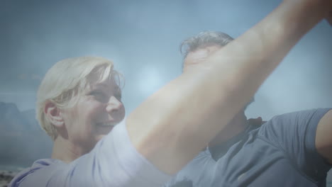 feliz pareja de ancianos caucásicos bailando en el campo, sobre nubes de rápido movimiento y rayos de luz