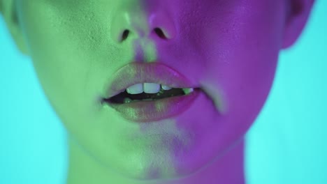 disparo de cerca de los labios de la mujer mientras la joven mastica una goma de mascar dulce y deliciosa contra un fondo turquesa con contraste púrpura verde en su cara en cámara lenta