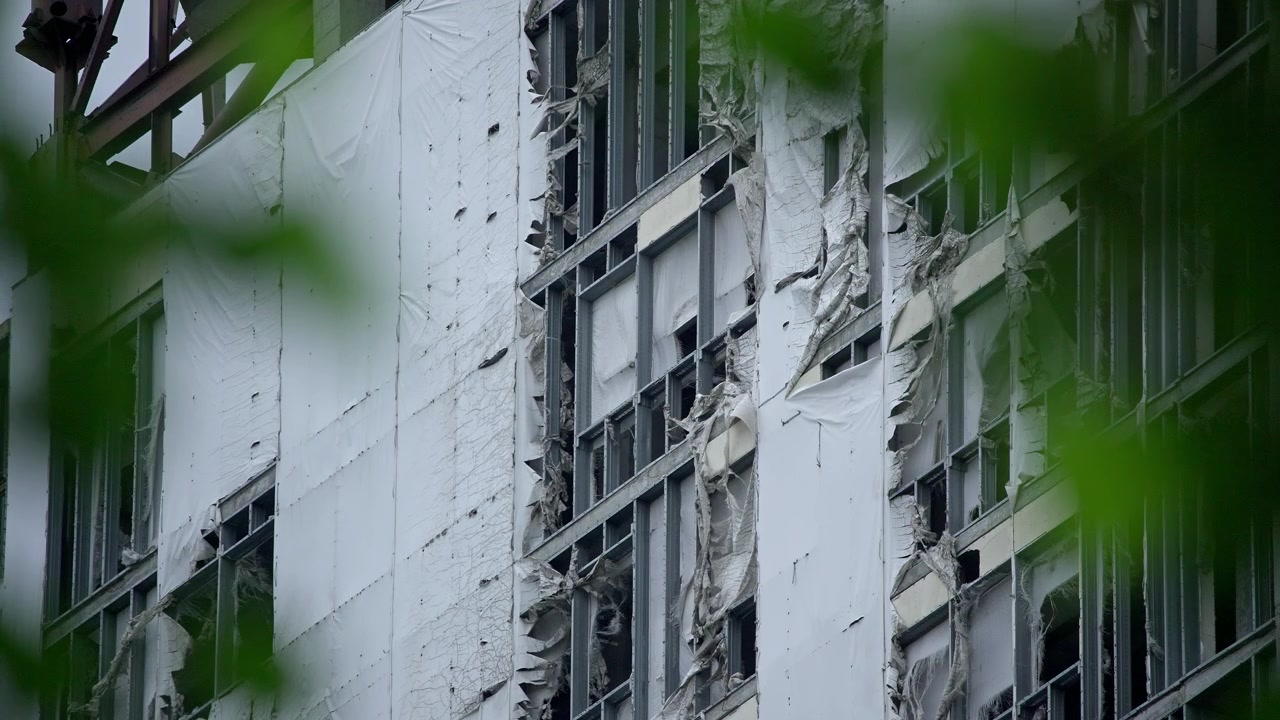 Facciata di edificio urbano con telo protettivo strappato e foglie verdi
