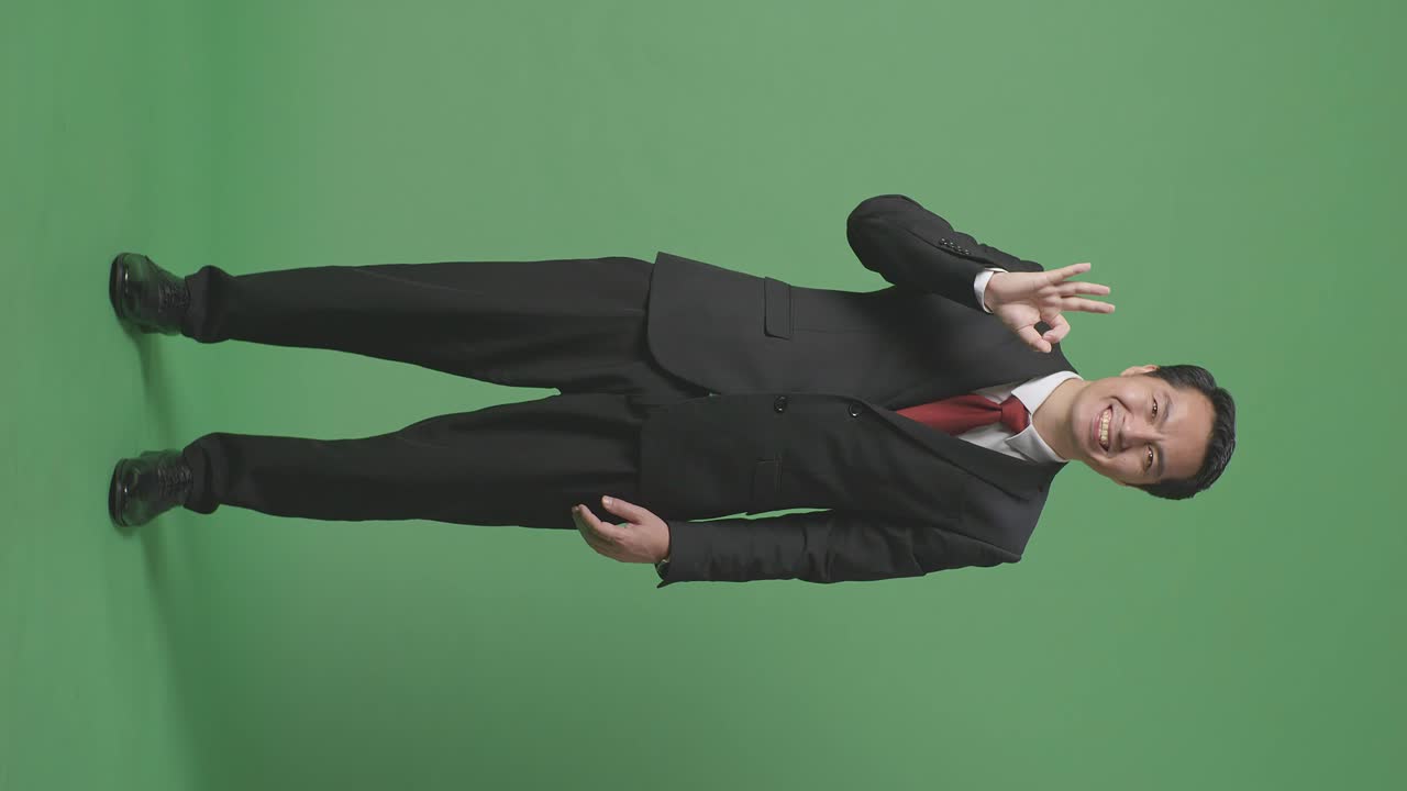 녹색 스크린 스튜디오에 서 있는 동안 한 몸짓과 미소를 보이는 아시아 사업가의 몸이 가득 차 있습니다.