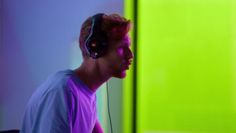 Excited-player-losing-game-in-neon-room-closeup.-Upset-man-taking-headphones-off