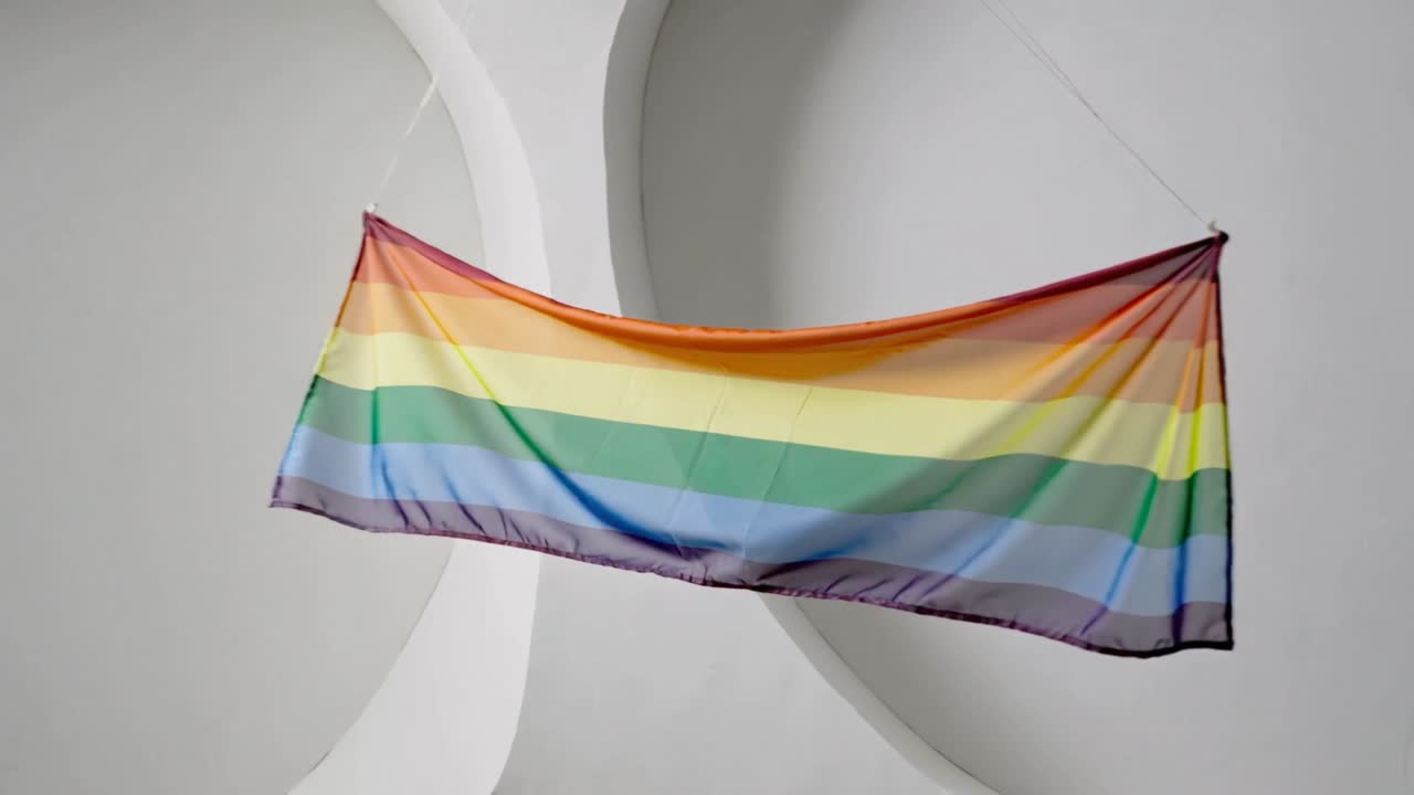 Tessuto a strisce arcobaleno che si sposta, ruota e si dispiega in galleria per una leggera brezza, sostenuto da cavi.