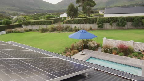 Casa-Con-Paneles-Solares-Y-Sombrilla-En-El-Jardín-En-Un-Día-Soleado.