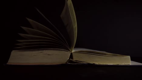 Slow-motion,-close-up-of-an-old,-vintage,-open-book-with-pages-turning-on-the-wind,-on-a-dark-room-with-few-light,-with-black-surroundings