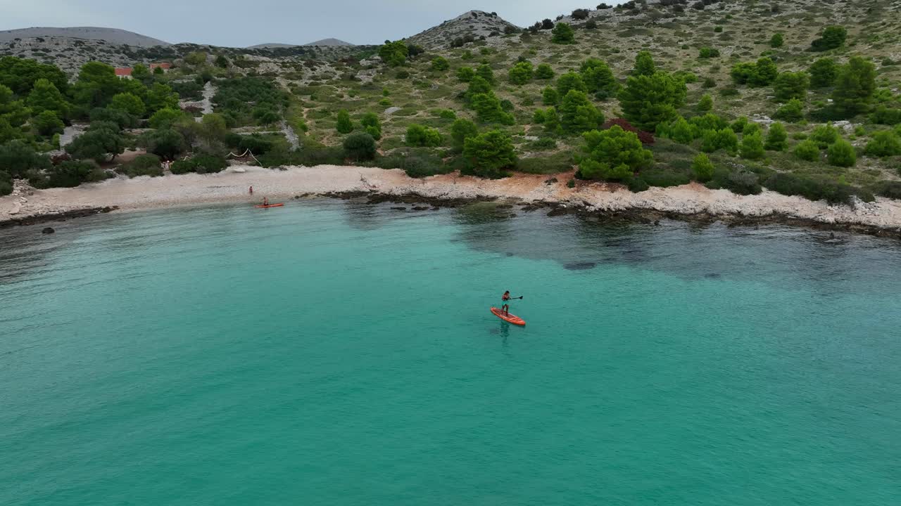 Aerial: man doing standup paddleboarding on the Mediterranean Sea during the day in the Kornati Bay, Dalmatia, Croatia, establishing drone shot