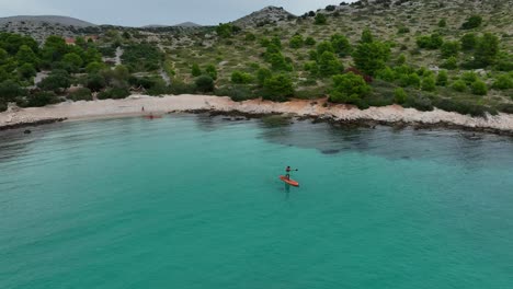 aerial: man doing standup paddleboarding on the mediterranean sea during the day in the kornati bay, dalmatia, croatia, establishing drone shot