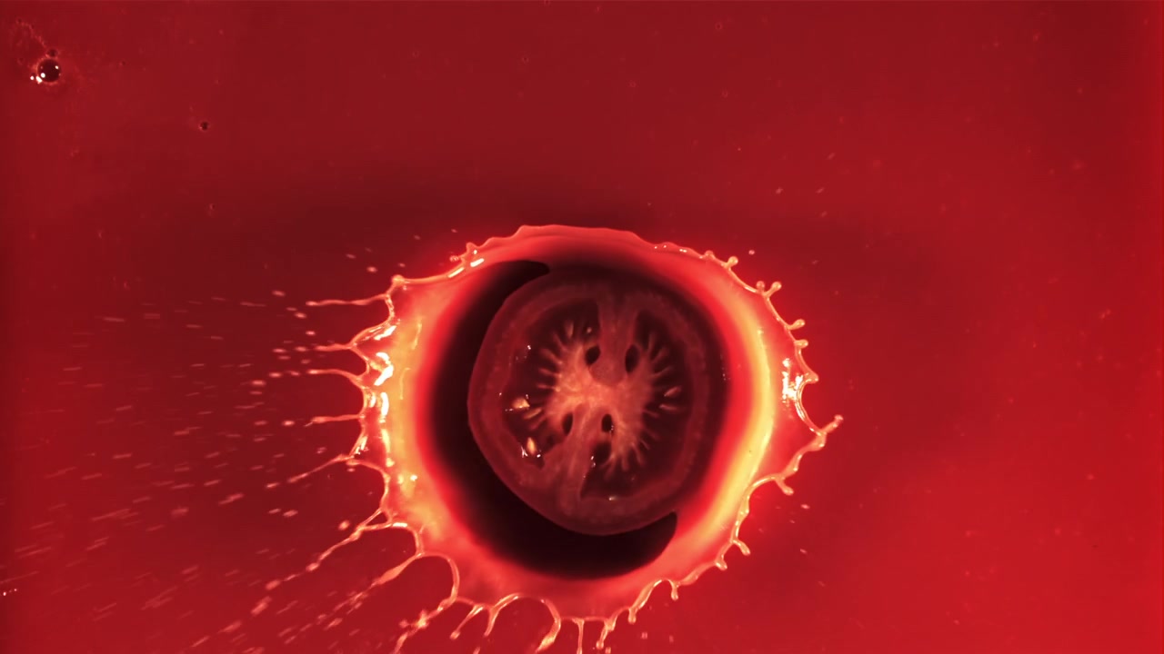 Fetta di pomodoro fresca che schizza in un liquido rosso al rallentatore.