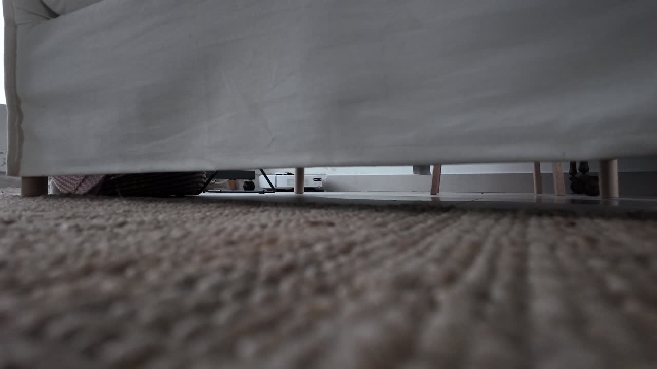 Slow-motion shot of an AI robotic cleaner moving under a bed on a carpeted floor