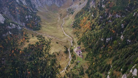 Autumn-colors-drape-the-Bucegi-Mountains-with-Malaiesti-Chalet-nestled-in-a-valley,-aerial-view