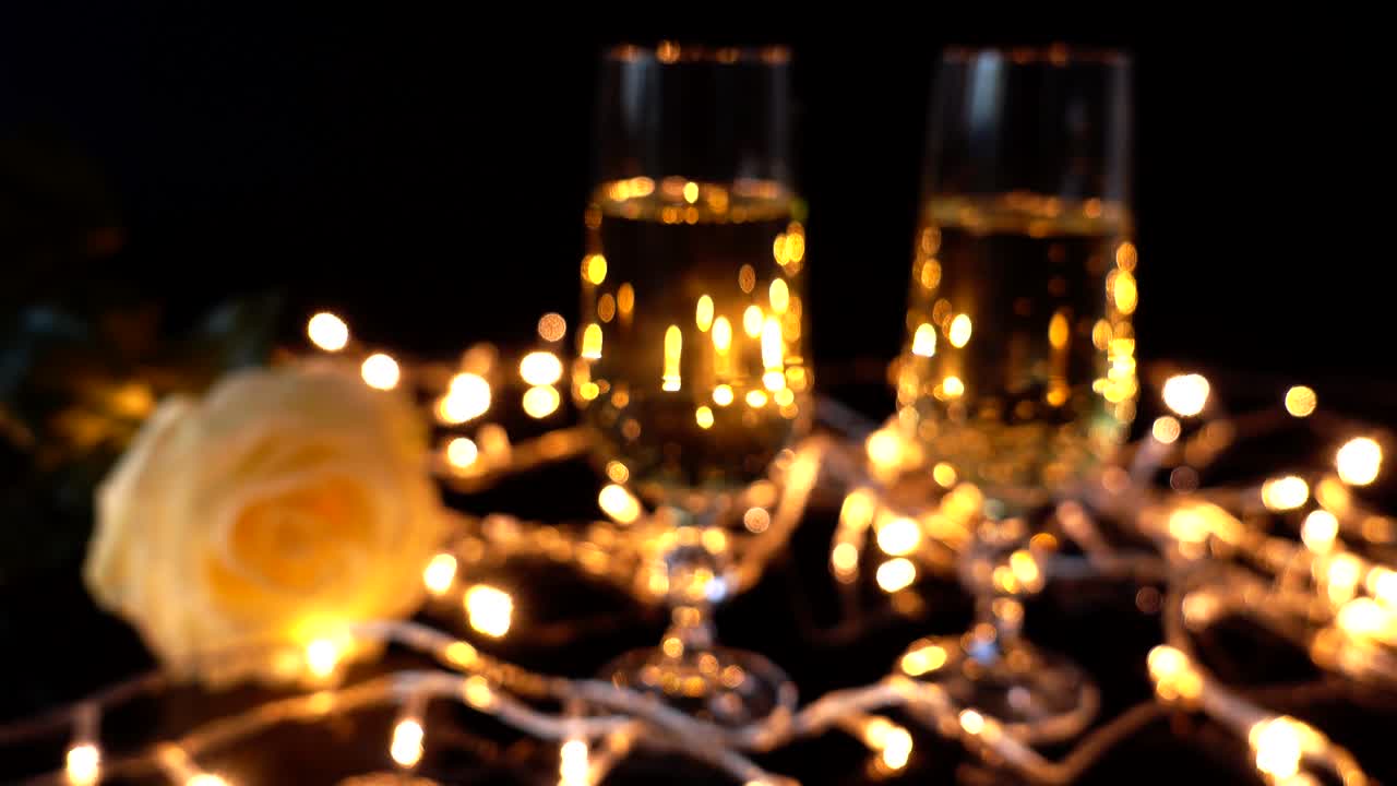 Gläser mit Champagner und Rosen vor dem Hintergrund heller Lichterketten. Unscharf