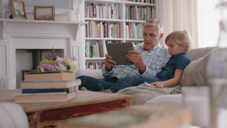 grandfather showing little boy how to use tablet computer teaching curious grandson modern technology intelligent child learning mobile device sitting with grandpa on sofa 4k