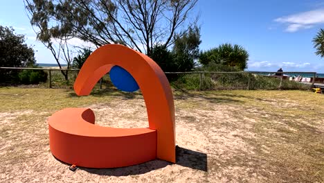 orange sculpture with blue accent in outdoor setting