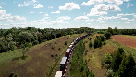 endless freight train travels through grassy valley landscape underneath bridge as car passes on road