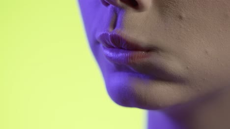 young-woman-eating-a-tortilla-chip,-chewing-mouth-close-up-shot-on-yellow-background,-pink-lighting