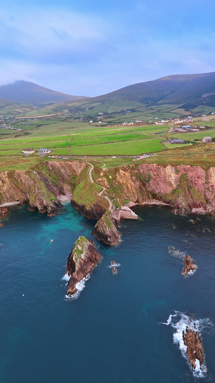 High dangerous cliffs descending into the blue waterscape. Vast valley with cottages scattered by the landscape at backdrop. Vertical video.