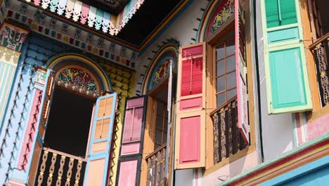 Vibrant, ornately decorated shophouse windows with open shutters in daylight, captured with upward camera movement and dynamic angles, highlighting architectural details