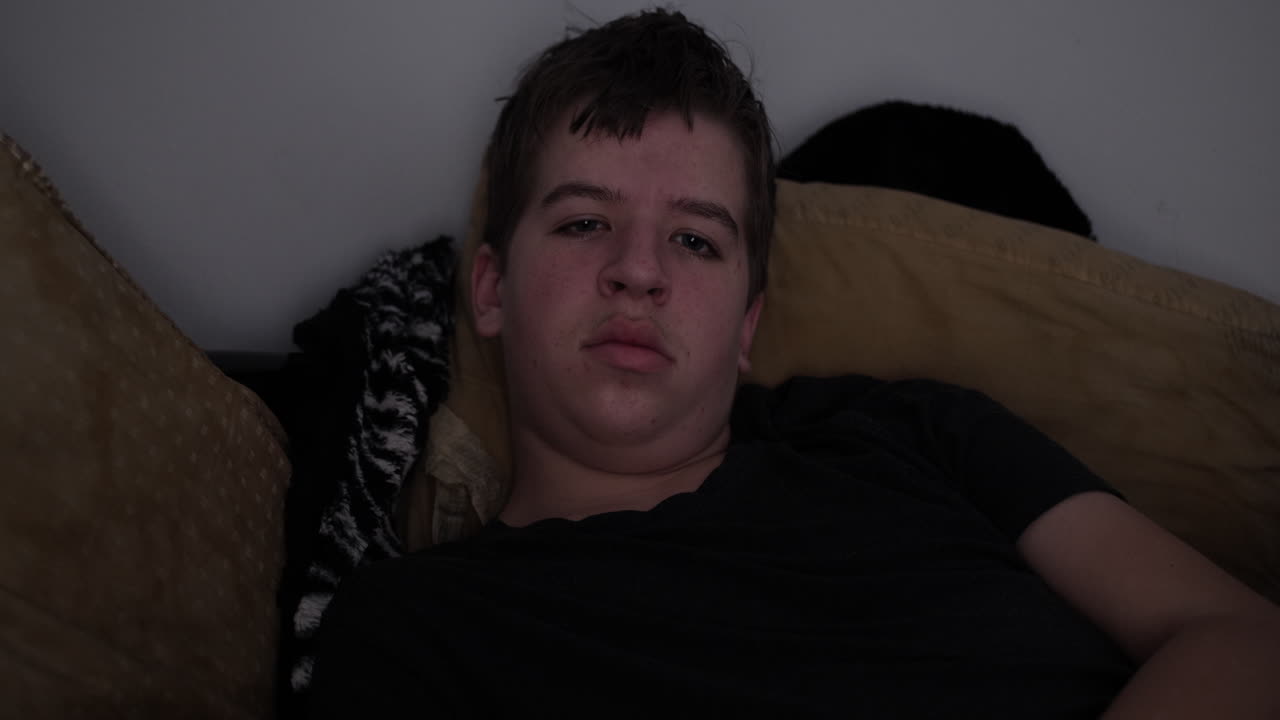 un joven adolescente de secundaria se acuesta en su cama viendo la televisión