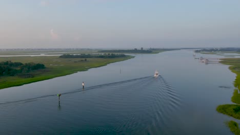 Vista-De-4k-De-Un-Barco-De-Arrastre-En-La-Vía-Fluvial-Girando-Para-Revelar-Un-Pequeño-Pueblo-De-Playa-Con-Un-Destello-De-Lente-En-La-Mañana