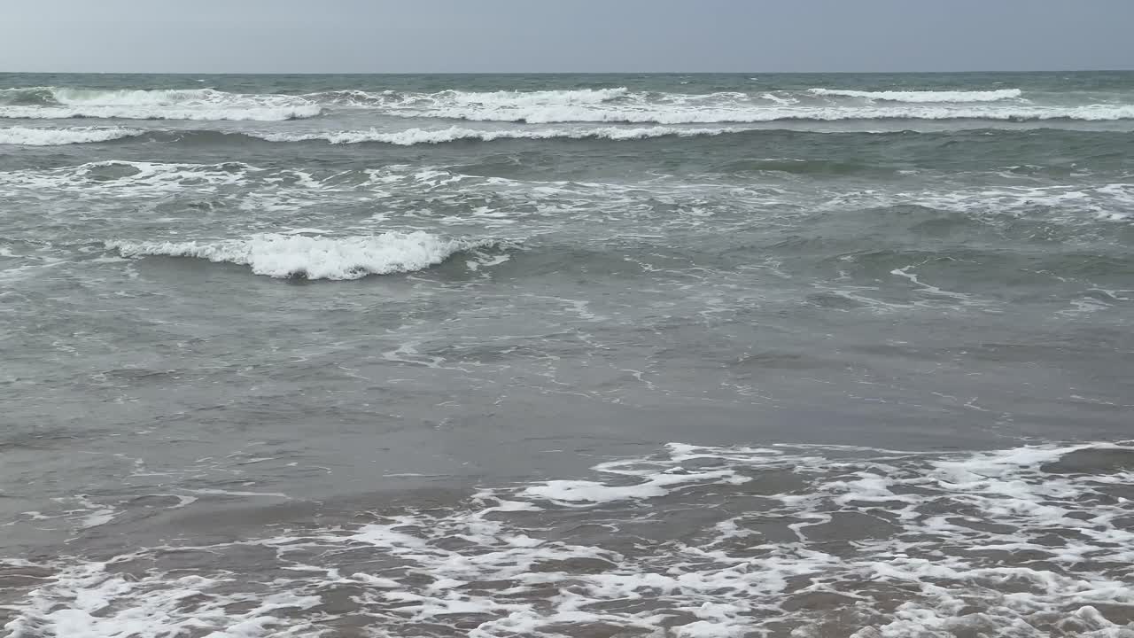 Dark ocean waves crashing against the shore on a cloudy day, creating a dramatic and moody atmosphere filled with the power and energy of nature's elements