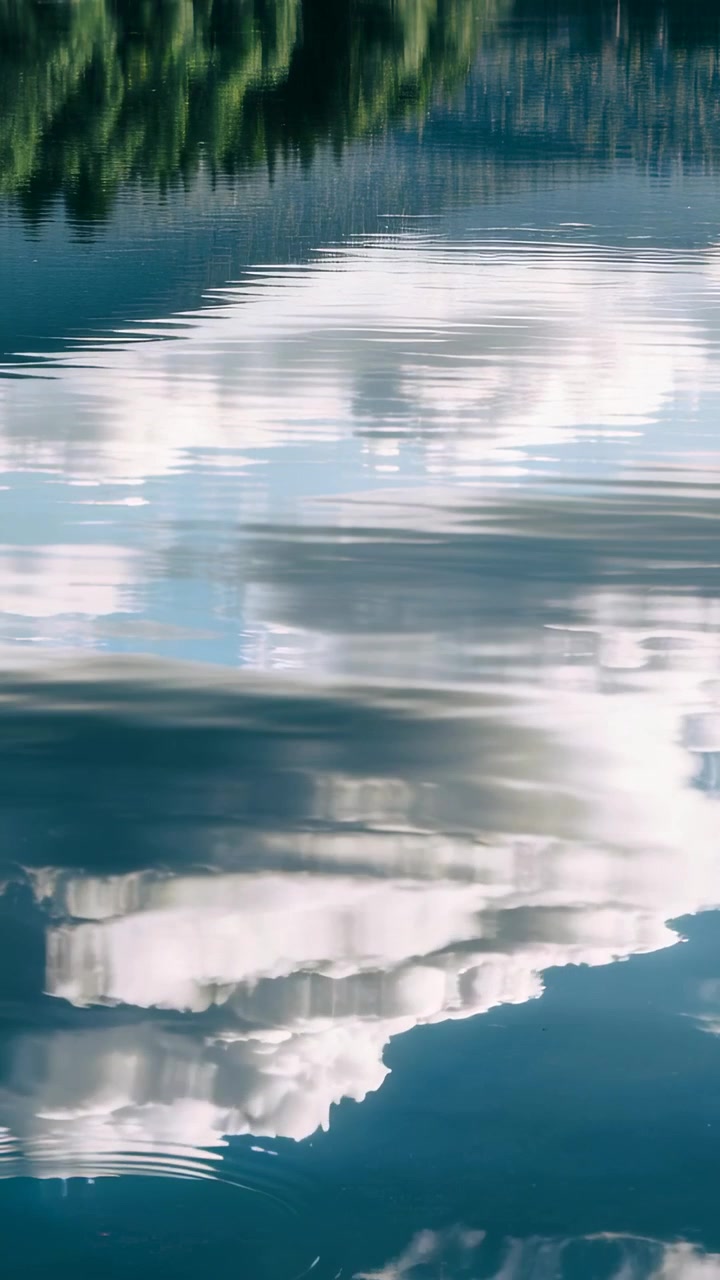 Vertical video: Rippling cloud reflection shifting on pond after ring ripples from left with trees