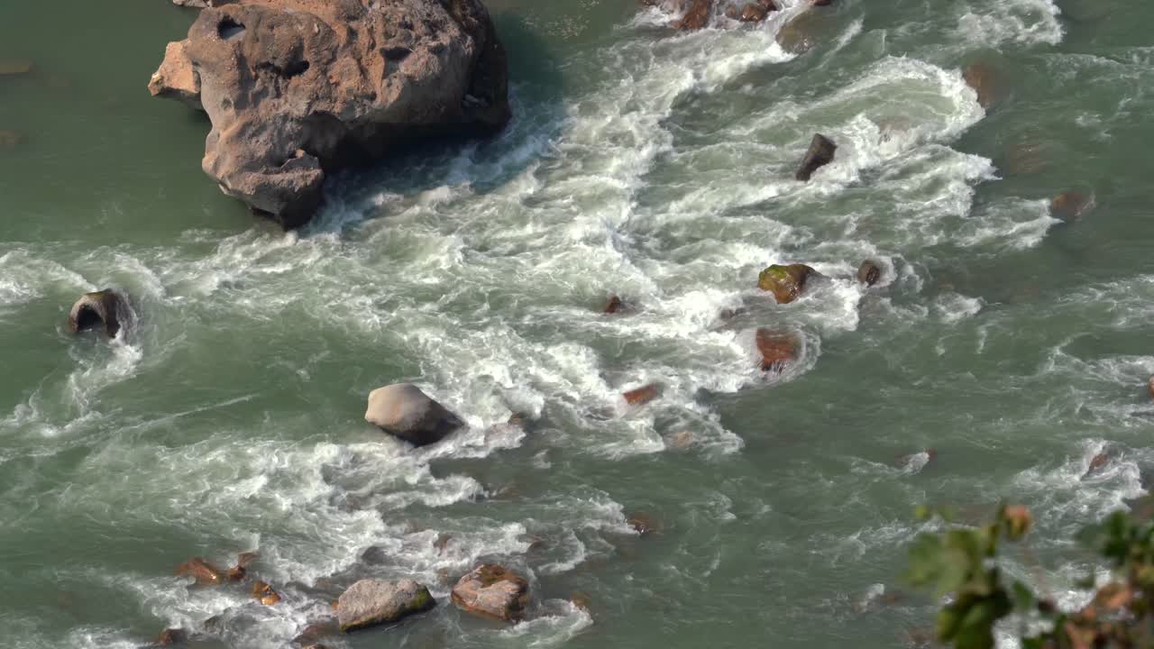 A high angle view looking down on the rapids and rocks in a river as the water flows.
