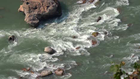 a high angle view looking down on the rapids and rocks in a river as the water flows.