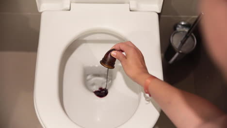 white young female hand emptying the blood of her menstrual cup in the toilet.