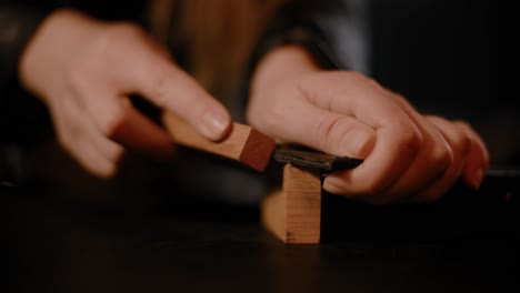 Woman-hands-sanding-the-edges-of-leather-product,-dark-setup,-high-contrast,-color-graded