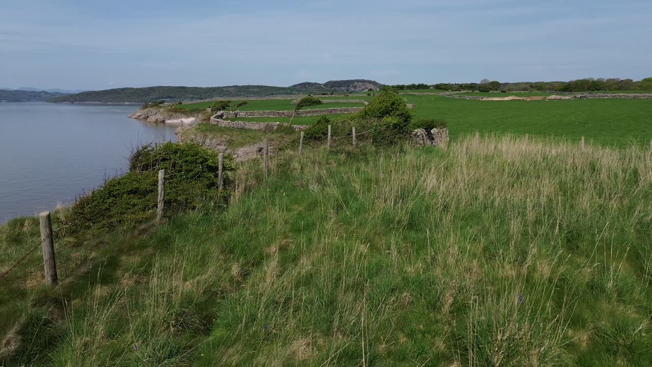 Aerial view over Lake district farmland passing wood and stone fenced grassy meadow over cliff edge
