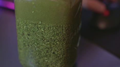 stirring yerba mate in a glass jar. close up shot of tea swirling in water with colorful background from a gamers desk. healthy green drink while playing games.