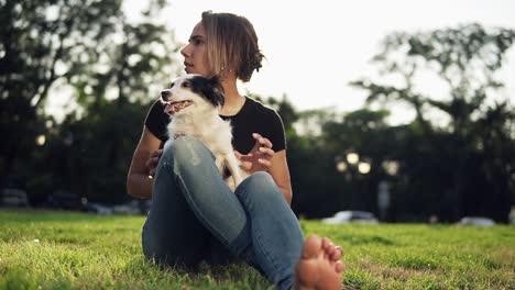 Junges-Schönes-Mädchen,-Das-Mit-Ihrem-Hund-Auf-Dem-Gras-Sitzt