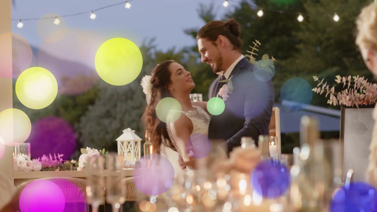 Bride and groom taking hands, dancing to celebrate marriage under lights, bokeh highlights floating