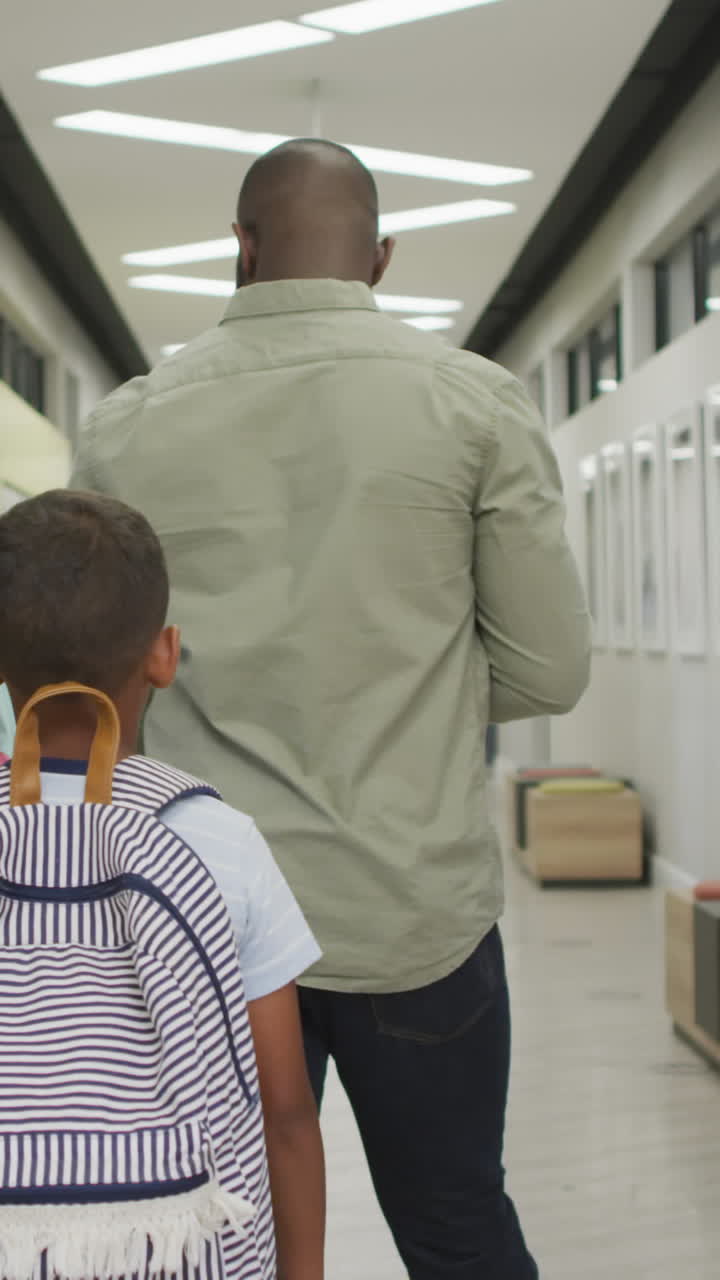 Video of back of african american male teacher and diverse pupils walking at school hall