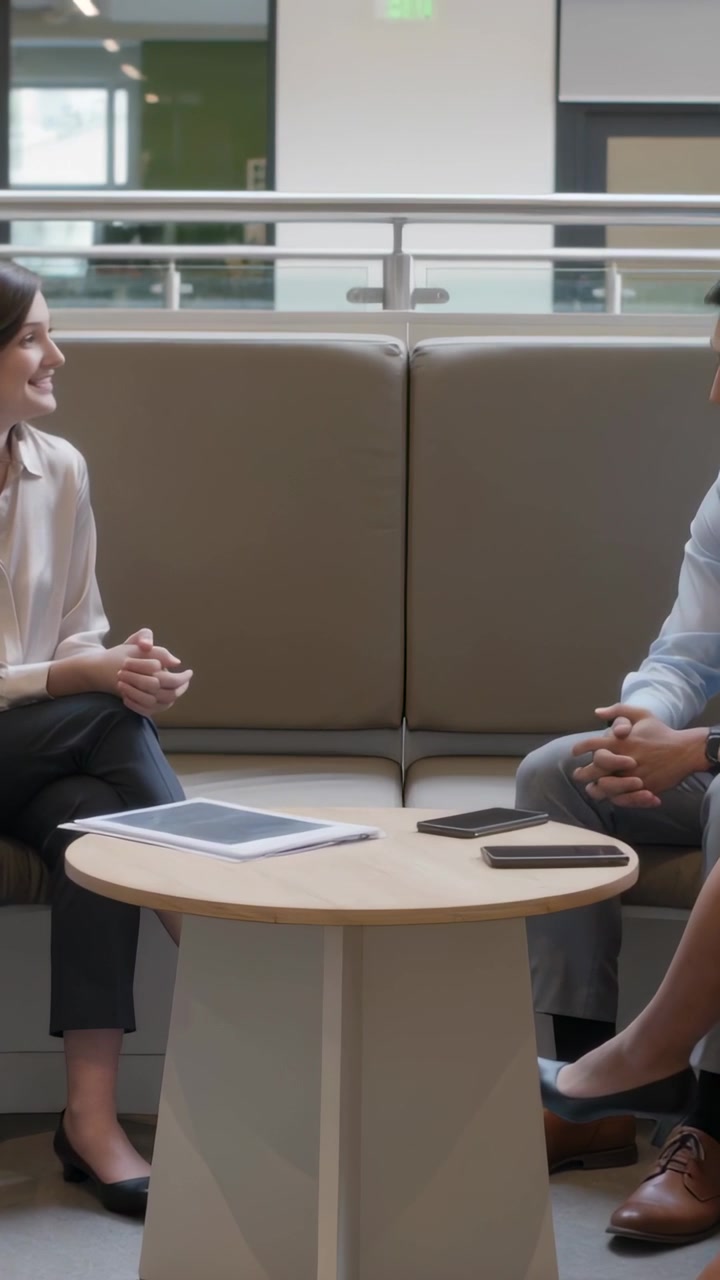 Video verticale: Una donna in camicetta inizia a condurre una discussione di lavoro, mentre un uomo annuisce in ufficio con un tablet.