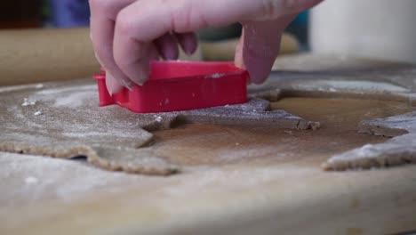 caucasian woman cutting gingerbread house out of dough