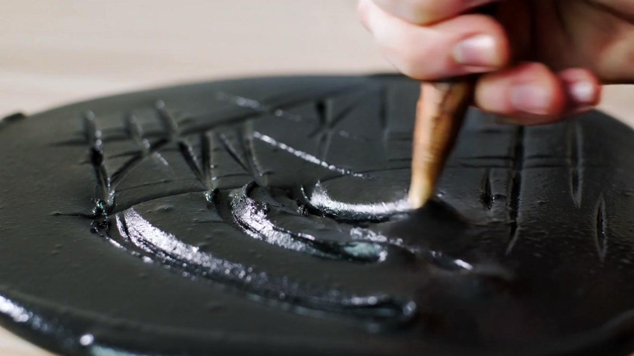 Stylus touching right hand carving curves on round glossy black slab on workbench, making texture