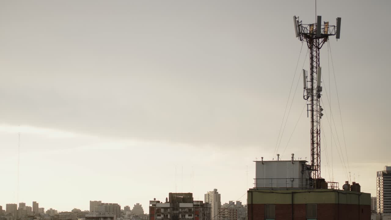 Cell tower stands tall on a rooftop in Buenos Aires against a hazy urban skyline at dusk