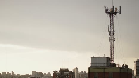 cell tower stands tall on a rooftop in buenos aires against a hazy urban skyline at dusk