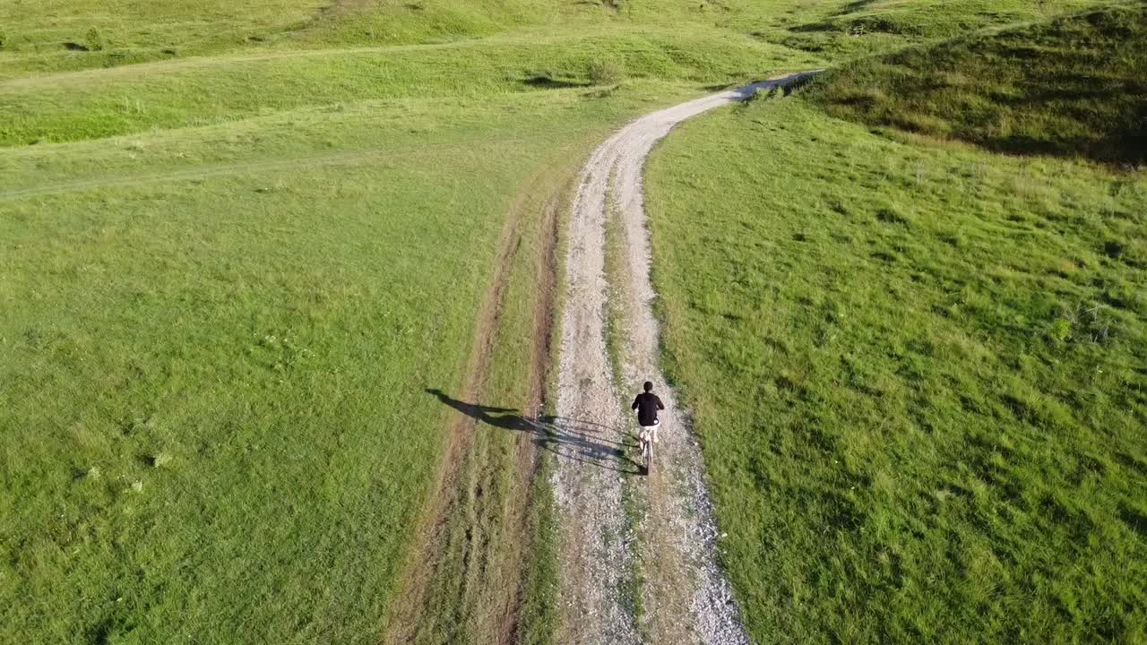 imágenes aéreas de un hombre montando su bicicleta en una carretera rural en un día soleado de verano