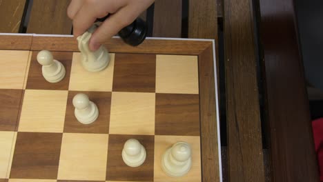 chess-top-down-view-white-pawn-capturing-black-bishop,-chess-board-on-wooden-table,-slow-motion