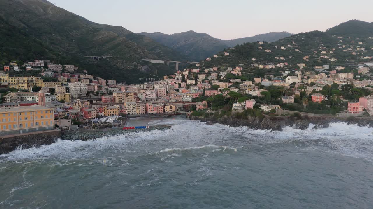 Onde marine che si infrangono sulla costa rocciosa con case nel porto della città di Genova