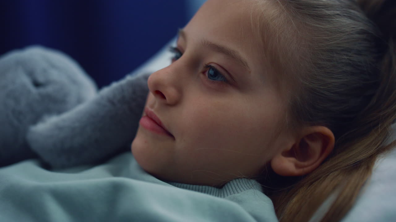 Portrait girl lying in bed with plush toy on hospital checkup in pediatric unit.