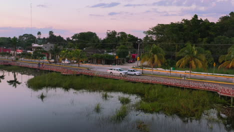 aerial-tracking-a-car-driving-on-a-road-through-Coba-town-near-lake-at-sunset-in-Mexico