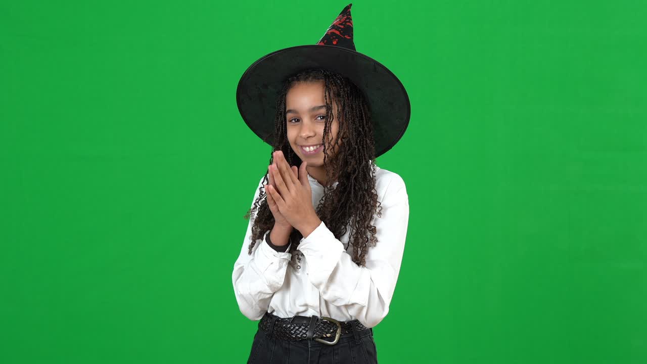 una adolescente afroamericana sonriente en el sombrero de bruja de halloween posando en el fondo de chromakey. adolescente despreocupado positivo en disfraz en la pantalla verde. concepto de vacaciones.