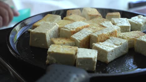 tofu cerrado siendo frito en hierro fundido ingredientes especiales para cocinar una comida dos latas de frijoles arroz plátano aguacate cebolla roja y cilantro