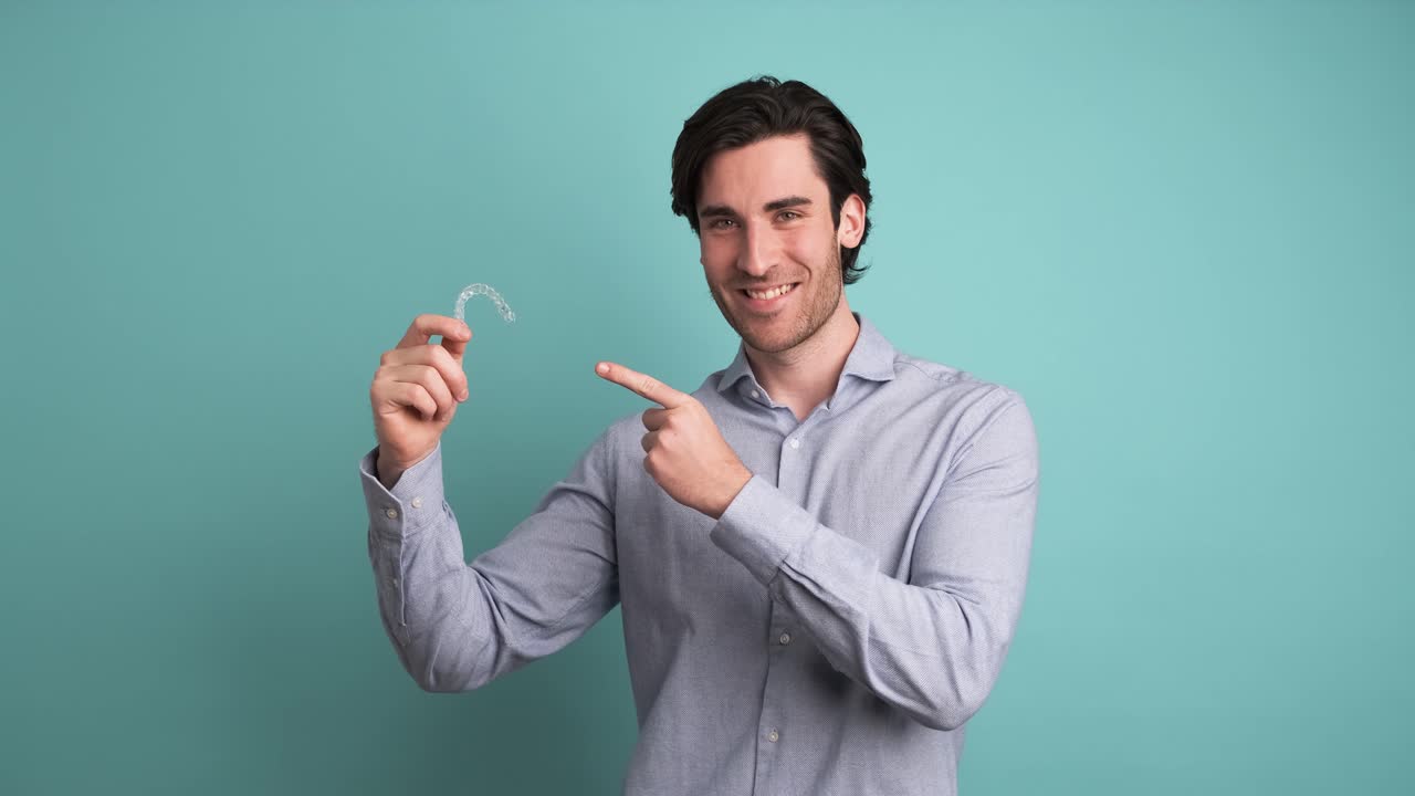 Happy man showing invisible braces in blue studio