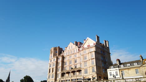 Pulteney-Weir-Y-El-Empire-Hotel-En-Bath,-Somerset-En-Una-Hermosa-Mañana-De-Verano-Que-Se-Desvanece-En-Diagonal-Hacia-Un-Cielo-Azul-Claro-Con-Una-Gaviota-Volando-A-Través-Del-Marco